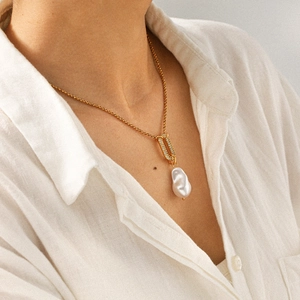 Gros plan sur pendentif perle baroque avec fermoir serti de diamants sur chaîne dorée