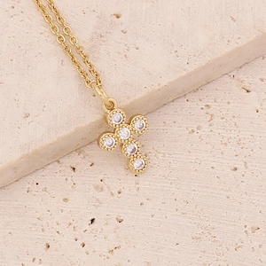 Macro shot of 18K gold plated cross pendant with cubic zirconia on a stone surface