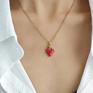 Élégant collier pendentif fraise doré avec émail rouge porté sur une chemise blanche