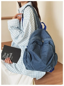 Detail of blue denim backpack with front zipper pocket and side compartments on model