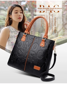Detail view of large black embossed tote bag with brown handles and gold hardware