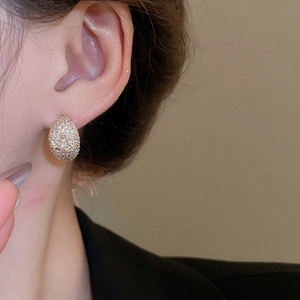 Close-up of elegant gold plated oval stud earrings with pavé crystals on ear