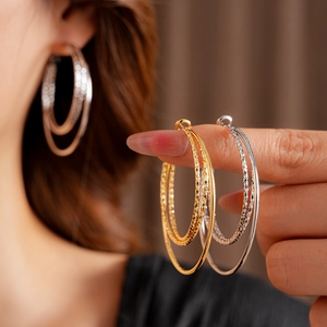 Detalle de pendientes de aro de doble capa texturizados en oro y plata en modelo y mano