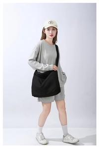Dettaglio di una borsa a tracolla in tela nera indossata da una modella in abito grigio casual