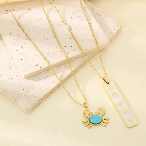Close-up of gold stainless steel crab pendant with blue stone and rectangle tag necklace