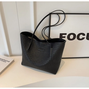 Detailed view of black woven texture tote bag with slim shoulder strap on desk
