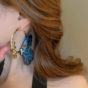 Detailed view of embroidery blue butterfly earrings with textured golden branch hoops