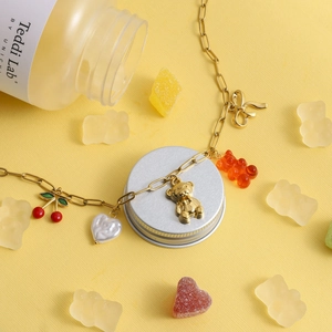 Detail of necklace featuring cherry, bear, and bow charms on a gold-plated chain