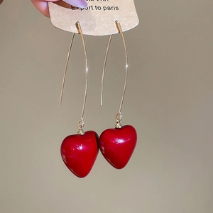 Detail of elegant gold hook earrings featuring glossy red heart-shaped pendants on a model