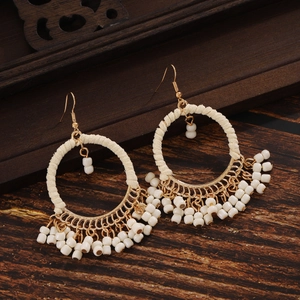 Detail of bohemian gold hoop earrings with white bead fringe on vintage wood background