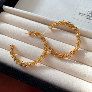 Detail shot of golden textured hoop earrings with a pleated surface finish in a jewelry box