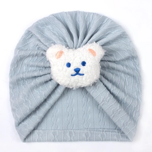 Close-up of baby knit turban hat featuring a 3D plush bear on soft blue fabric