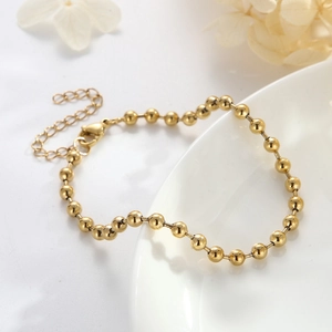 Minimalist golden stainless steel bead chain bracelet on a decorative ceramic plate