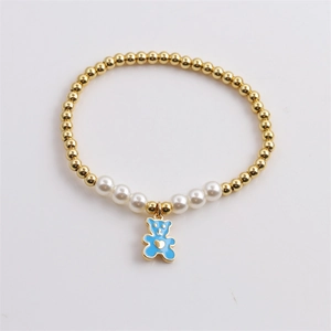 Detail eines Perlenarmbands mit Goldperlen, weißen Perlen und einem blauen Bärenanhänger