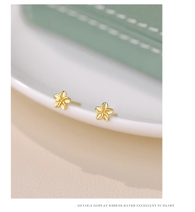Macro detail of gold-plated silver flower stud earring on elegant ceramic surface