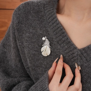 Detail of a silver feather brooch with zircon and mother of pearl on a grey knit sweater