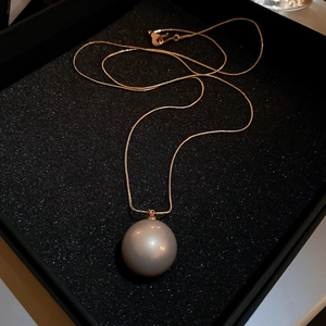 Vue détaillée du collier doré avec pendentif perle grise dans son coffret à bijoux noir