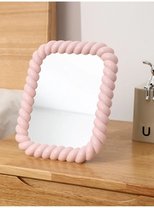 Detail of pink twisted frame desk makeup mirror on a warm wooden tabletop