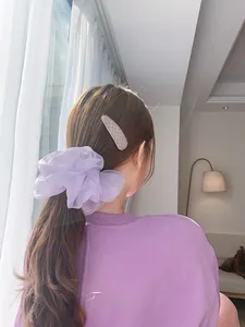 Detail view of a large purple organza scrunchie and grey hair clip on a model