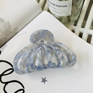Détail d'une pince à cheveux marbrée bleu-gris sur un fond blanc au style minimaliste