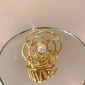 Detail of a gold floral hair claw clip with a white pearl on a reflective mirror surface