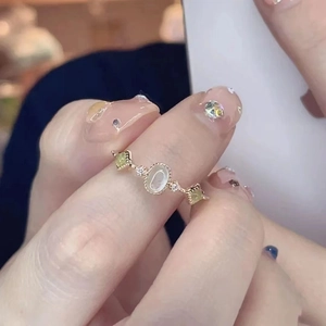 Elegant gold ring with white oval gemstone and green accents on woman's finger