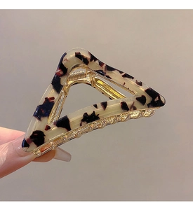 Detail showing the golden metal base and tortoiseshell acetate texture of the triangle clip