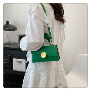 Détail du sac bandoulière vert en cuir avec boucle dorée et bandoulière en tissu plissé