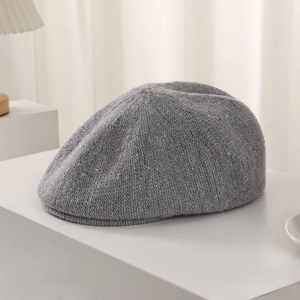 Detailed close-up of grey knitted beret with subtle silver sequins on white surface