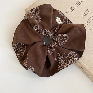 Detail of dark coffee paisley scrunchie with matte suede texture and branded button tag