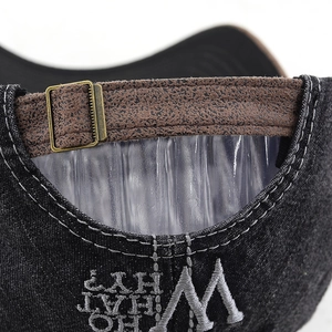 Detail of black denim baseball cap with leather strap, metal buckle and white embroidery