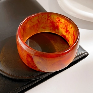 Close-up of retro amber resin bangle with marbled texture on leather and ceramic background