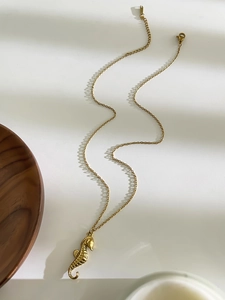 Détail d'un collier avec pendentif hippocampe doré sur un fond blanc minimaliste