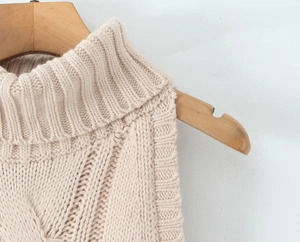 Close-up of neckline and shoulder detail on a beige knitted dress hanging on a wooden hanger
