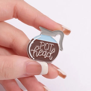 Creative coffee pot enamel pin with POT head text shown on a hand for scale