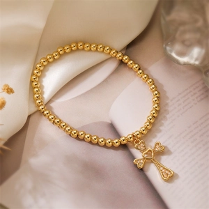 Macro detail of gold beaded bracelet featuring a micro-set zircon heart cross pendant