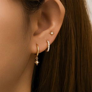 Close-up of gold starburst earrings set with zircon studs and hoop on a model ear