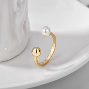 Gold open ring with white pearl and gold bead accents on white ceramic background
