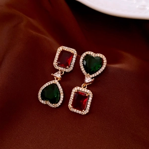 Close-up of vintage flower earrings with red and green gems on dark satin fabric