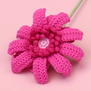 Nahaufnahme einer handgehäkelten Gerbera in Dunkelrosa mit detaillierter Garnstruktur