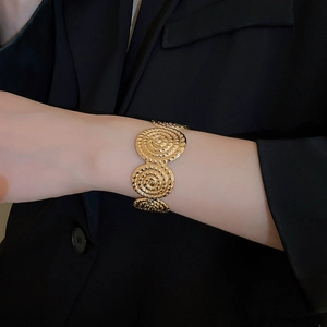 Close-up of golden spiral disc bracelet with textured metallic finish on a black suit sleeve