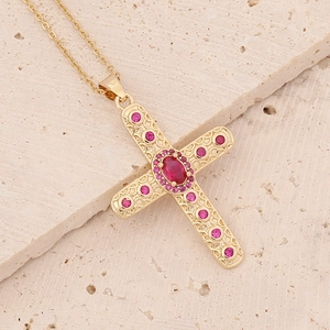Detail view of 18K gold cross pendant with pink zircons on a beige stone surface