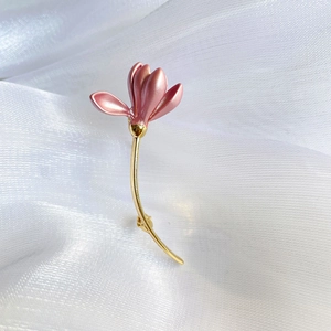 Detailed close-up of a pink floral enamel brooch with gold stem on white silk fabric