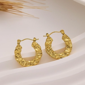 Close-up of golden C-shaped hoop earrings with hammered metal texture on white stand