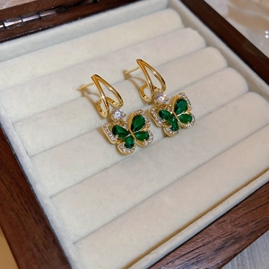 Macro shot of gold butterfly earrings featuring emerald stones and sparkling zircons
