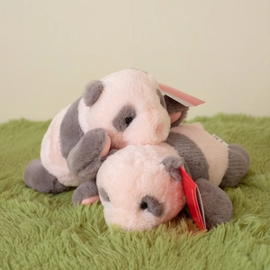 Pair of cute plush panda dolls in soft pink and grey faux fur lying on green grass