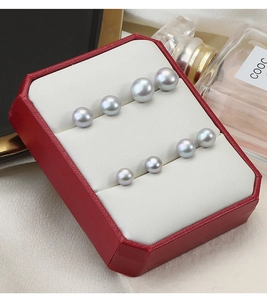 Macro view of four different sized grey pearl earrings in a red velvet jewelry box