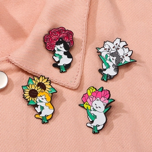 Set of four cute enamel cat pins holding colorful flowers on a pink denim backdrop