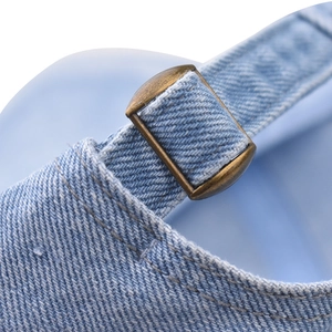 Macro view of adjustable brass buckle on light blue washed denim baseball cap