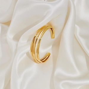Detailed close-up of a polished triple-layer 18K gold-plated cuff bracelet on white silk